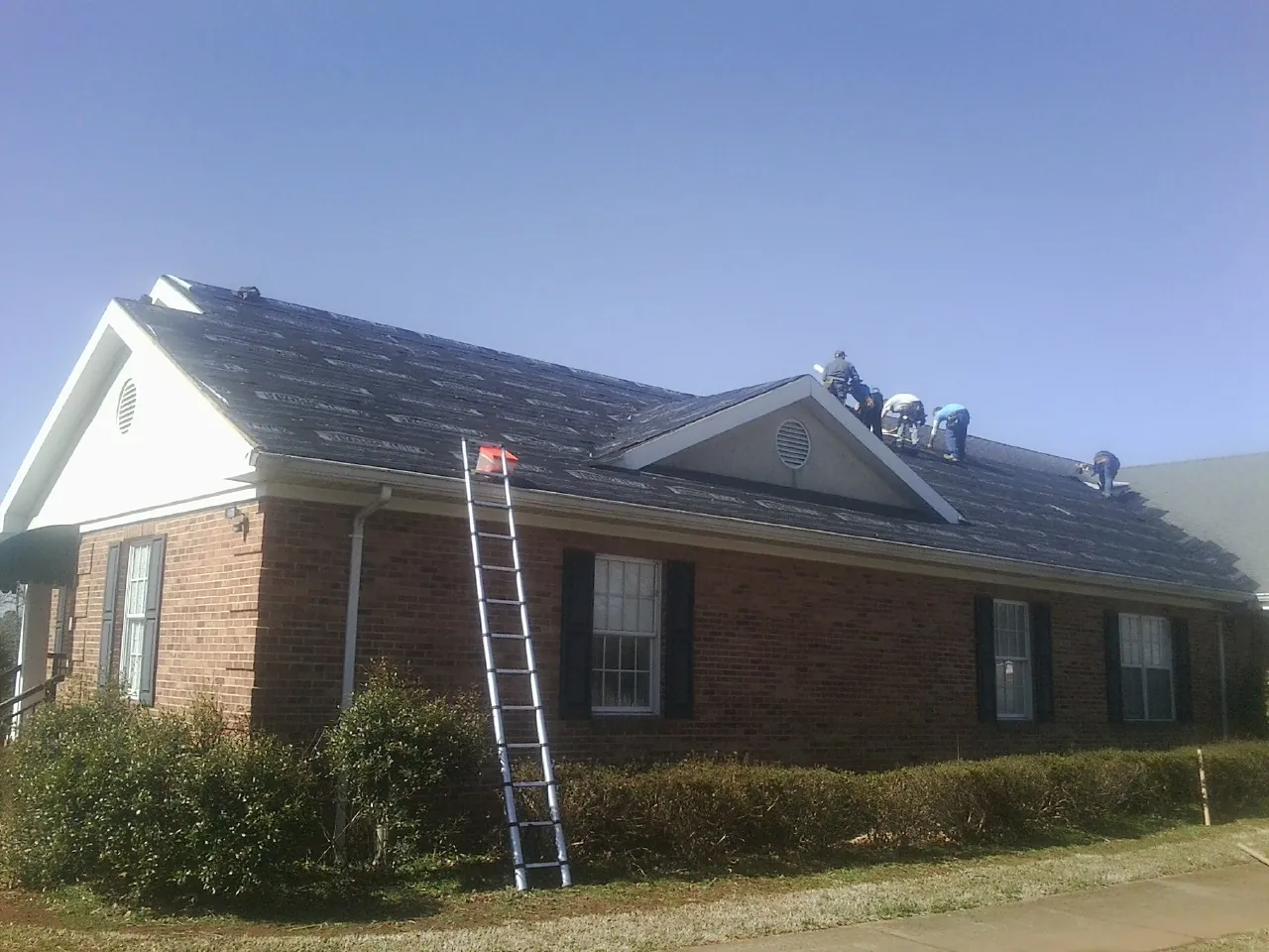 Crew tearing shingles off a brick ranch roof with a ladder set — Emergency Roof Repair work by our crew in Mountain Home