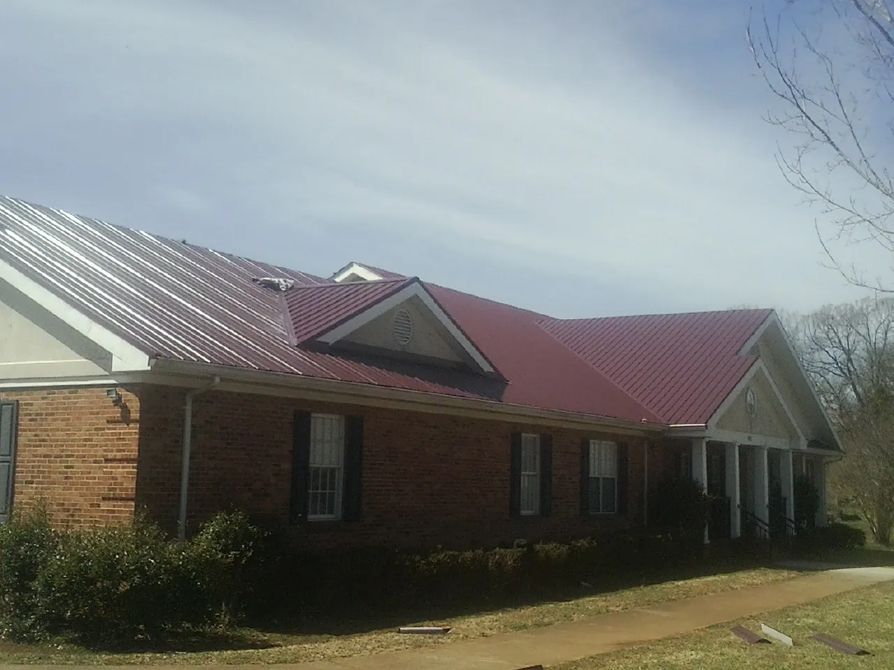 Red metal roof with gabled entries on a long brick building, from a Hail Damage Roof Repair job in Mountain Home