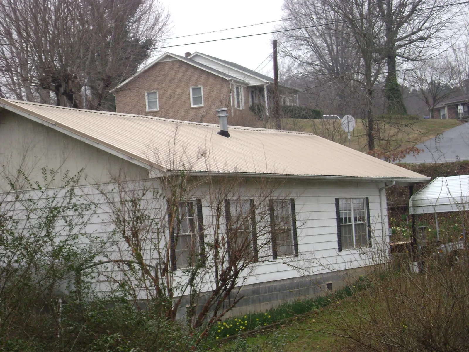 Tan metal roof on a white sided house set into a hillside — Commercial Roofing by Roofing Brothers in Mountain Home